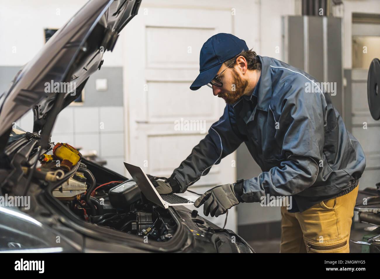 Un mécanicien qualifié répare une voiture avec l'aide d'un diagnostic informatique. Photo de haute qualité Banque D'Images