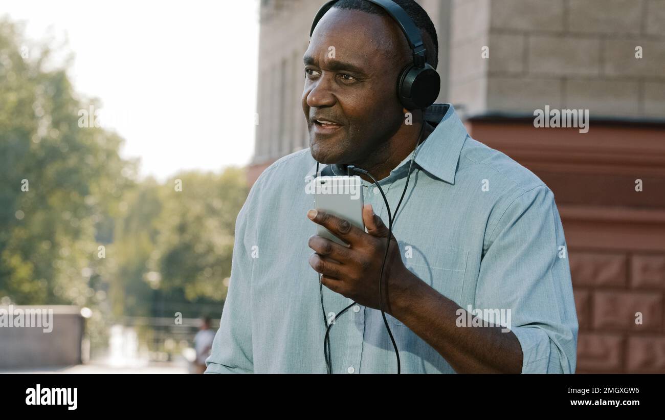 Emotionnel senior Africain américain homme écoutant de la musique dans des écouteurs appréciant la chanson audio application de téléphone mobile dans la ville à l'extérieur. Heureux mûr Banque D'Images