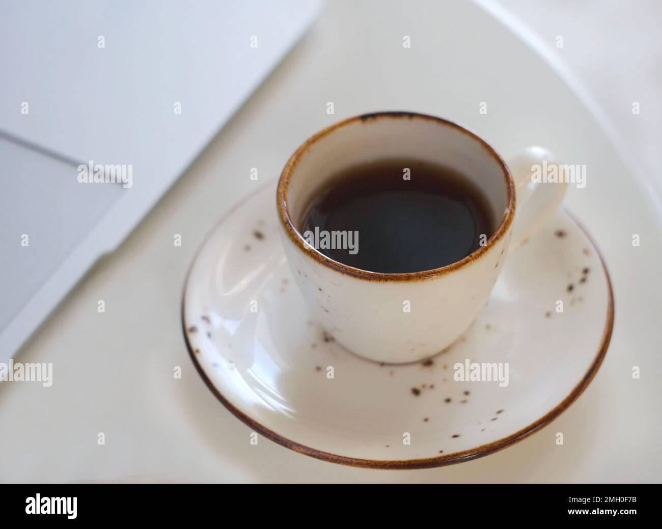 Une tasse de café noir parfumé est placée sur une table blanche. Derrière se trouve un ordinateur portable Banque D'Images