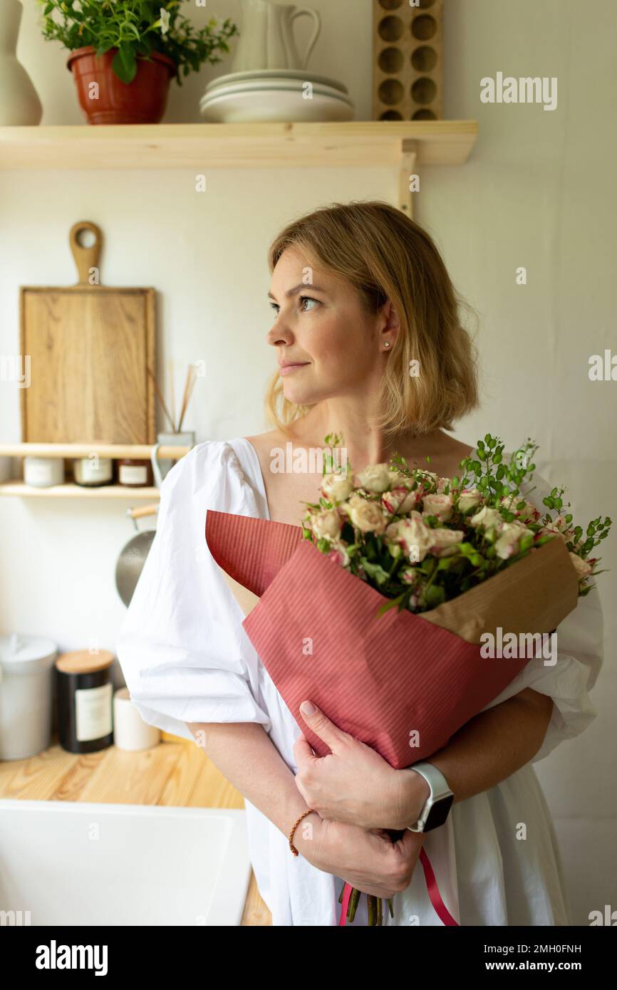 Une femme d'âge moyen se tient dans la cuisine avec un bouquet de fleurs Banque D'Images