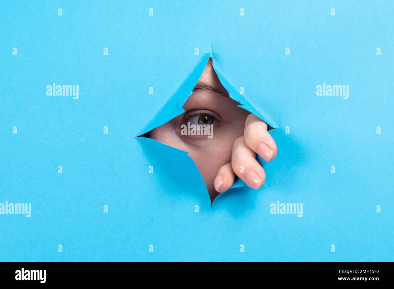 Une femme piquant hors de trou dans fond de papier bleu. Banque D'Images Une femme piquant hors de trou dans fond de papier bleu. Banque D'Images