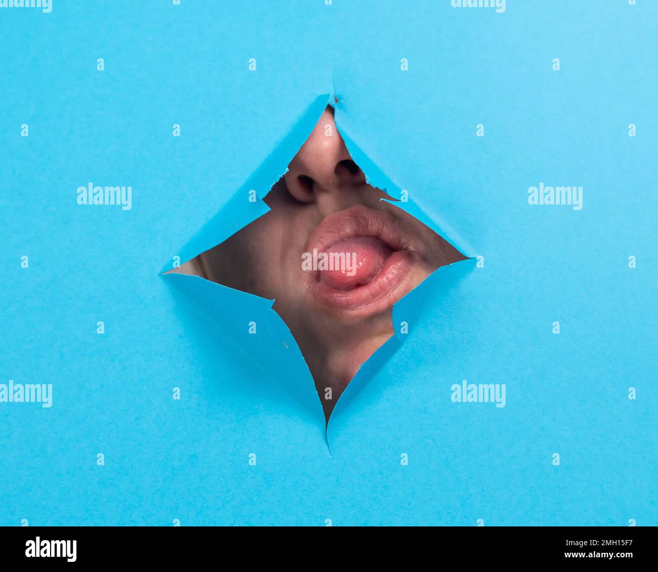 Femme qui colle sa langue hors d'un trou sur fond de papier bleu. Banque D'Images Femme qui colle sa langue hors d'un trou sur fond de papier bleu. Banque D'Images