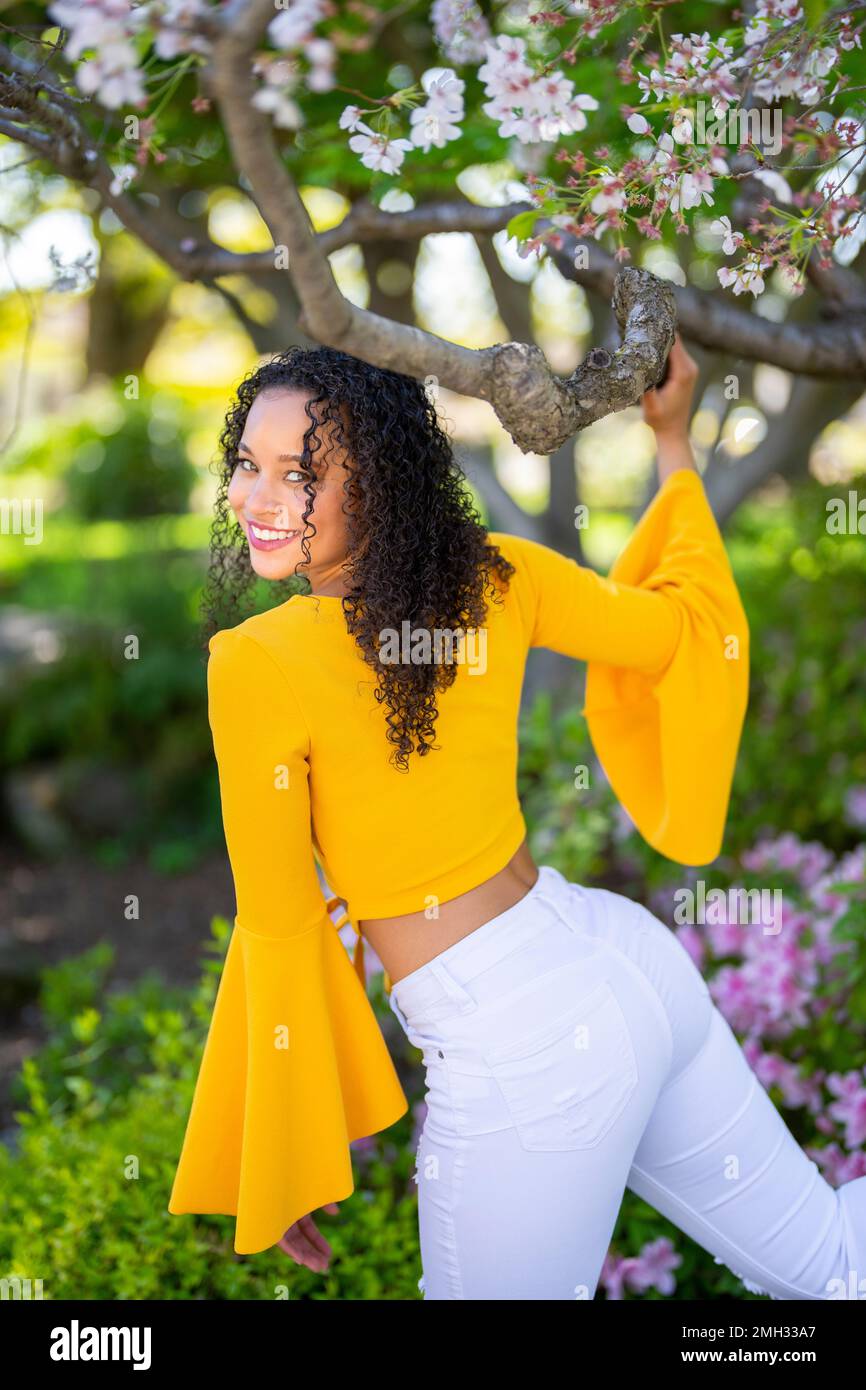 Vue de l'arrière 3/4 Portrait de corps de la jeune femme afro-américaine Kicking Leg Back and Holding Blossom Cherry Tree Branch - Printemps Banque D'Images