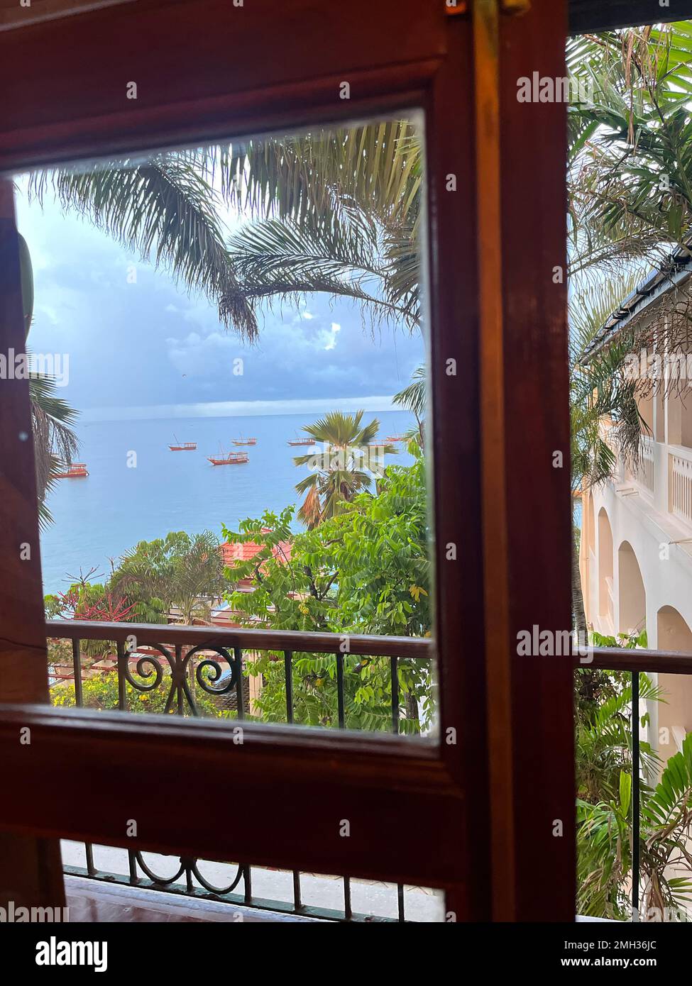 Une belle vue depuis une chambre d'hôtel. Vue fenêtre sur une plage bleue avec des bateaux à voile et quelques palmiers et plantes situés à Zanzibar, Tanzanie. Banque D'Images