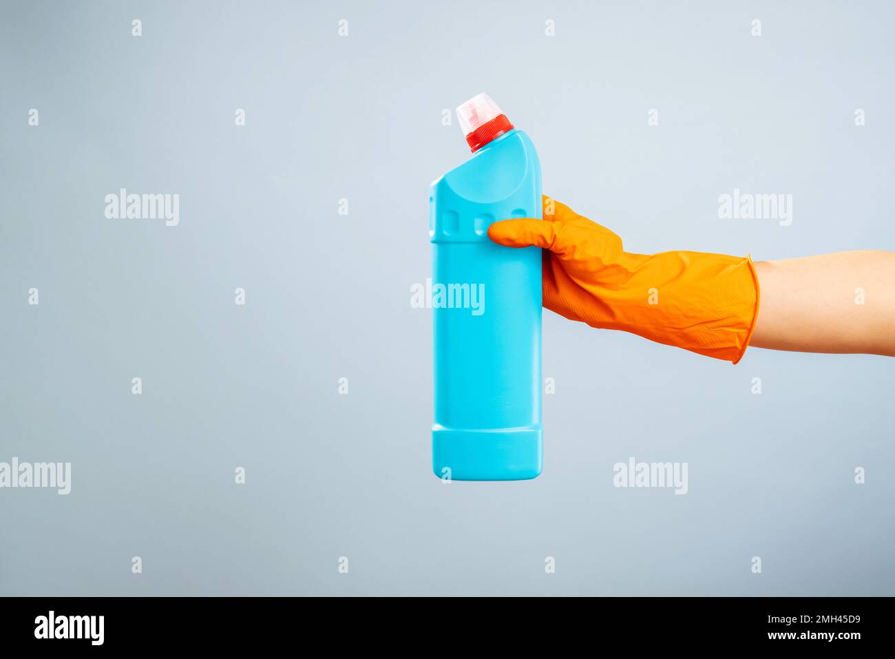 Main dans un gant tenant une bouteille de détergent en plastique sur fond bleu Banque D'Images