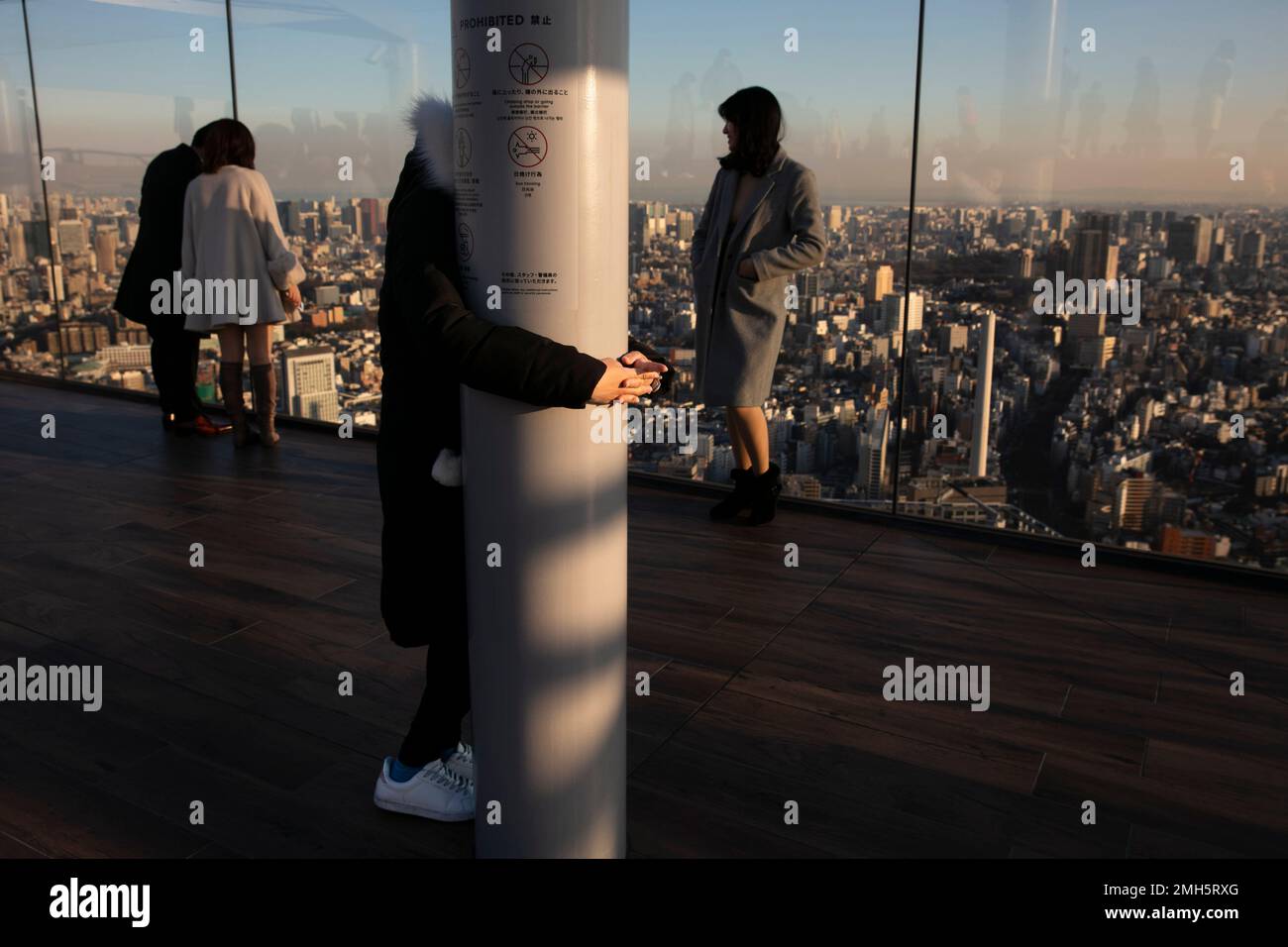 A tourist, who said she is afraid of height, clings to a pillar while her friends take pictures at Shibuya Sky observation deck Monday, Jan. 20, 2020, in the Shibuya district of Tokyo. Located on the rooftop of Shibuya Scramble Square, a 47-story high-rise that opened in November, 2019, the observatory is Tokyo's newest open-air observation deck, overlooking the famous Shibuya scramble crossing.(AP Photo/Jae C. Hong) Banque D'Images