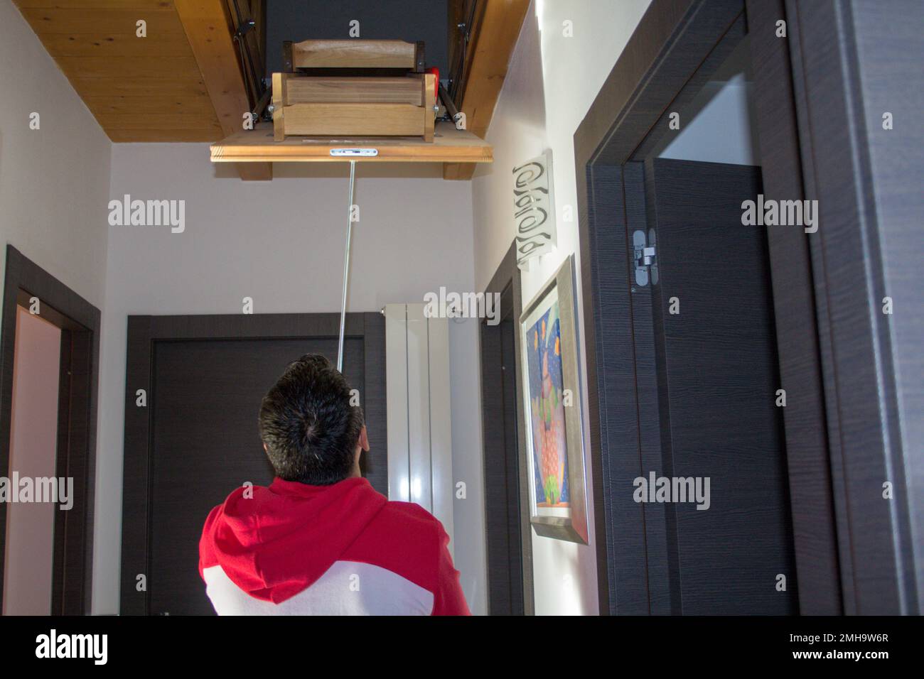 Image d'un homme à la maison ouvrant une échelle rétractable pour aller jusqu'au grenier. Optimisation des espaces intérieurs de la maison. Banque D'Images