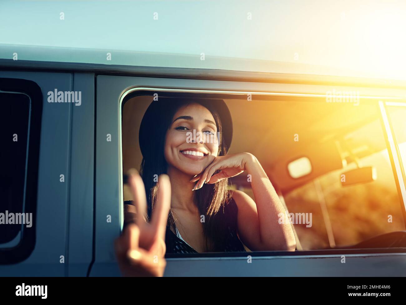 Bon voyage. une jeune femme s'est penchée hors de la fenêtre d'un minibus et montrant un signe de paix sur un voyage. Banque D'Images