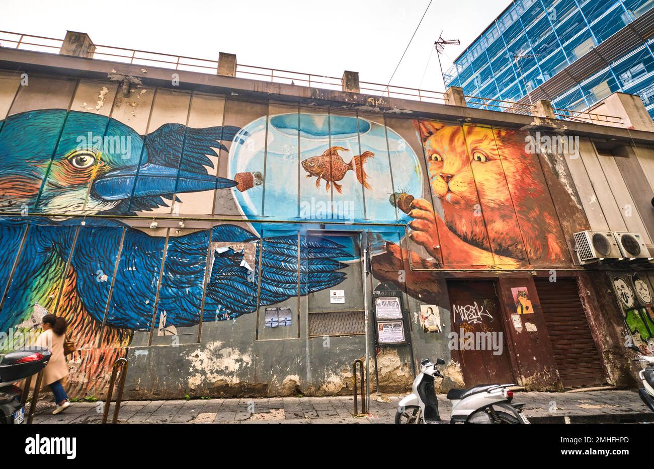 Une grande murale sur le côté d'un supermarché, représentant un oiseau bleu et un chat orange regardant un poisson rouge dans un bol de poisson. Un exemple de graffiti à Naples Banque D'Images