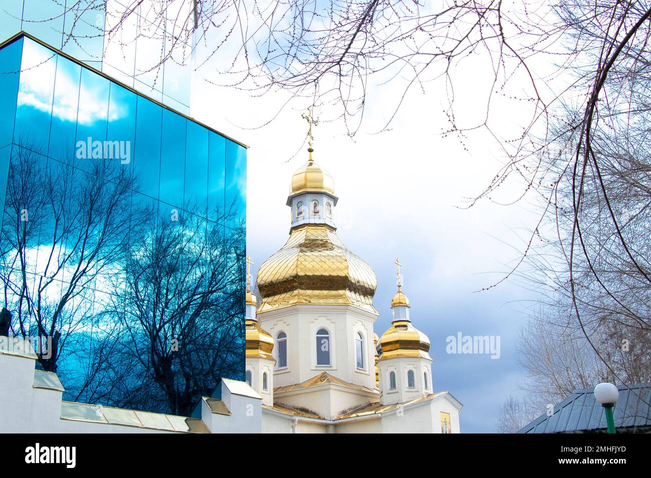 Reflet de branches d'arbres dans la façade d'un bâtiment en verre bleu et d'une église chrétienne en Ukraine Banque D'Images