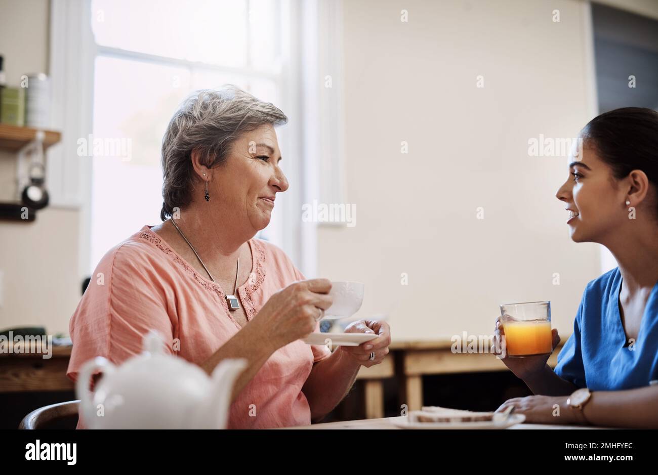 Le thé est toujours servi avec un côté de chat de chit. une jeune femme soignante attirante discutant avec un patient âgé dans une maison de soins infirmiers. Banque D'Images