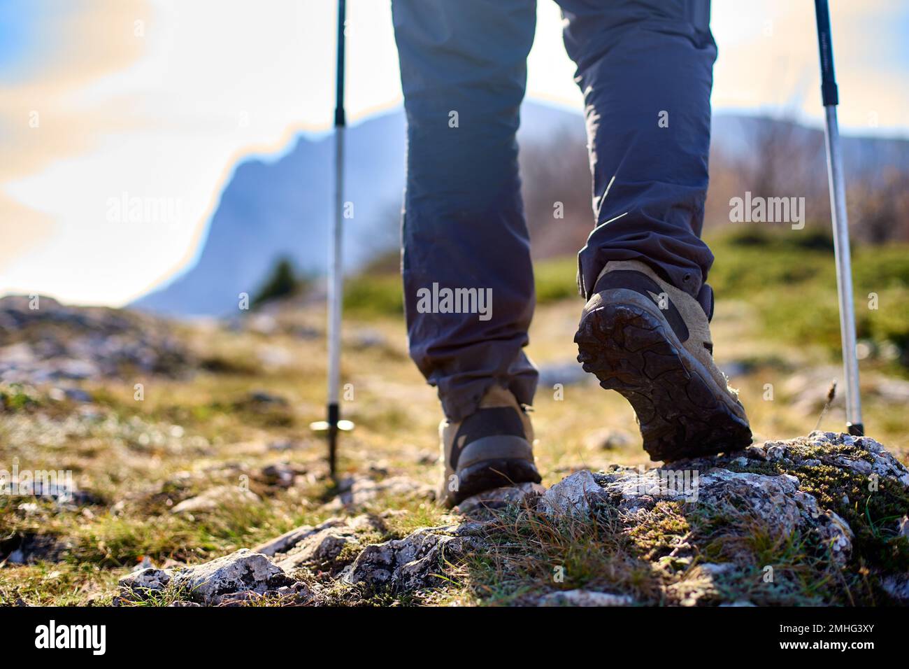 Jambes d'un randonneur dans des bottes de trekking marchant dans les montagnes avec des bâtons de marche nordique gros plan. Pieds de tourisme de marche portant des chaussures de randonnée avec Banque D'Images