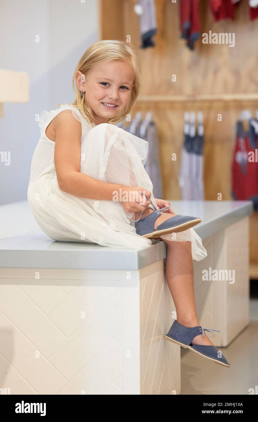 Petite fille, sourire de portrait et attacher la dentelle de chaussure sur la table dans le magasin de détail pour la mode ou le style de tout-petit mignon. Joyeux adorable enfant souriant pour faire du shopping Banque D'Images