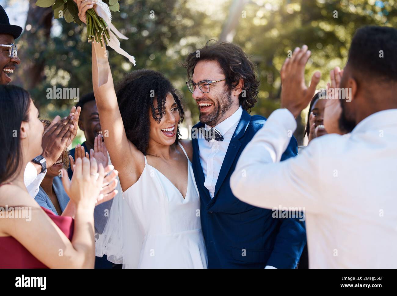 Bonne mariée et marié célébrer le mariage avec des applaudissements excités et joyeux dans la foule des invités. Amour interracial et bonheur de couple au mariage Banque D'Images