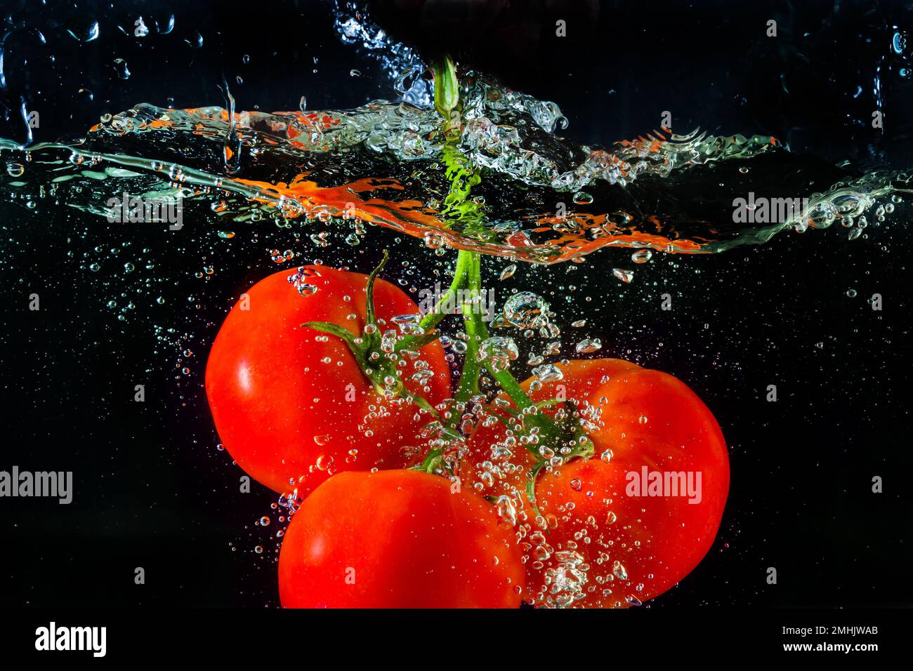 Tomate rouge fraîche tombant dans l'eau avec des éclaboussures d'eau et des bulles d'air isolées sur fond noir. Banque D'Images