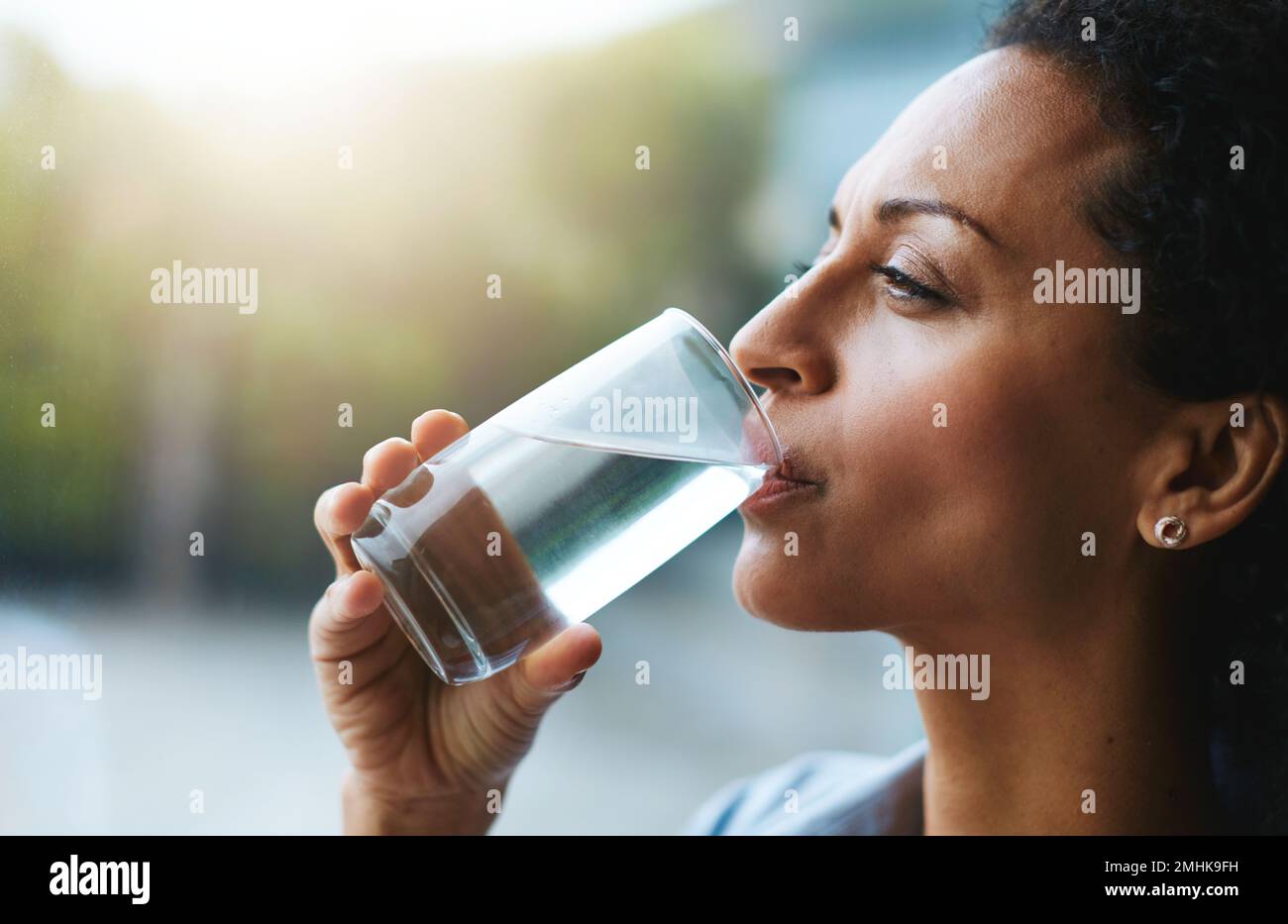L'hydratation est son secret de beauté. une femme boit un verre d'eau à la maison. Banque D'Images