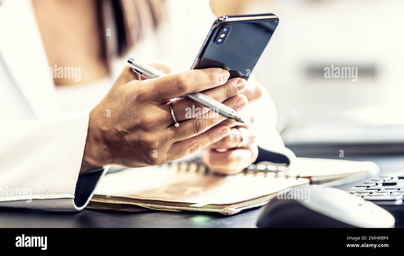 Mains d'une femme responsable avec un téléphone mobile, communiquant avec ses collègues pendant les heures de travail, envoyant des messages ou recevant des informations professionnelles. Banque D'Images