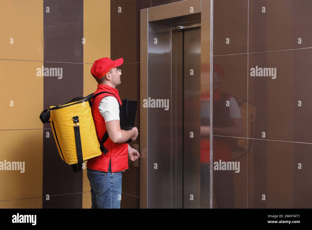 Messagerie mâle avec sac thermo et presse-papiers en attente de l'ascenseur. Service de livraison de nourriture Banque D'Images