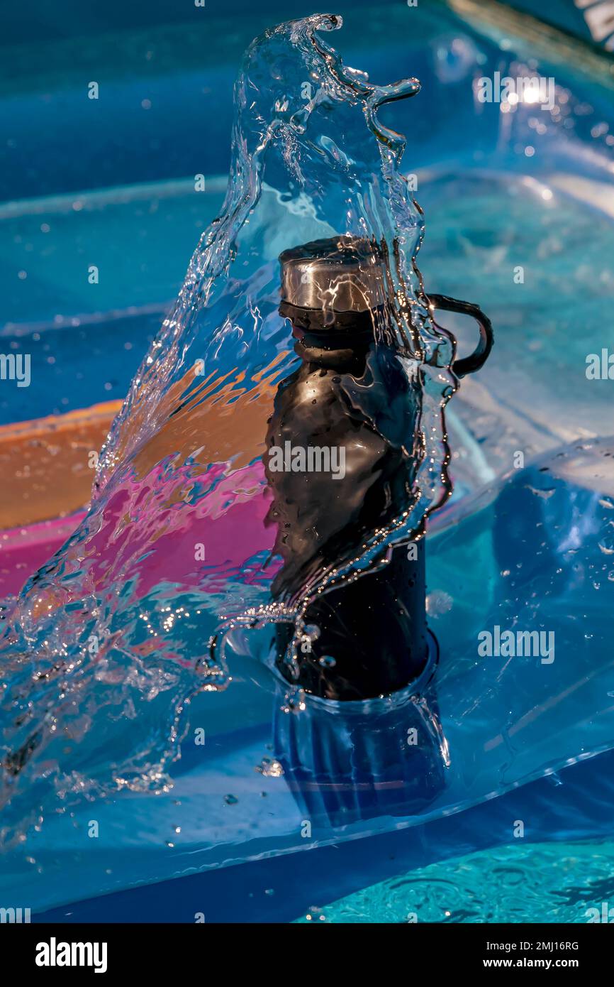 Une bouteille d'eau noire sur un matelas gonflable est lavée par une vague Banque D'Images