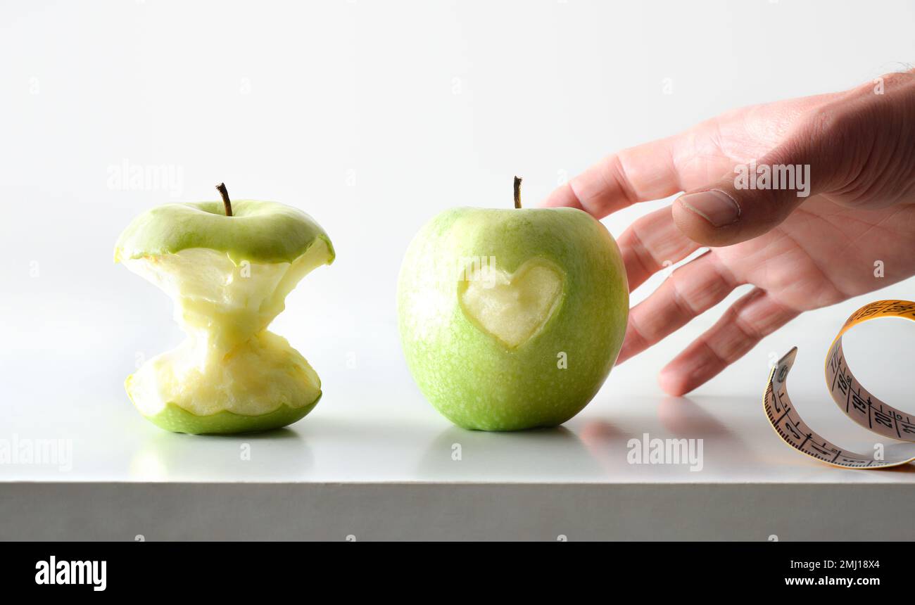 Action de manger des pommes pour la santé avec la main cueillant pomme avec coeur avec la moitié de pomme mangée et mètre ruban avec fond blanc isolé. Avant v Banque D'Images