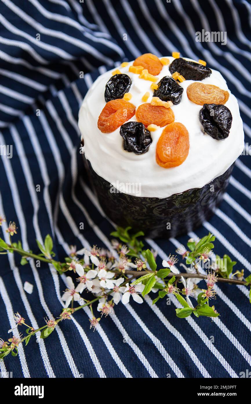 Le gâteau de Pâques, décoré d'abricots et de pruneaux séchés, se dresse sur un tablier bleu rayé, une branche fleurie. Concept de vacances religieuses de Pâques Banque D'Images