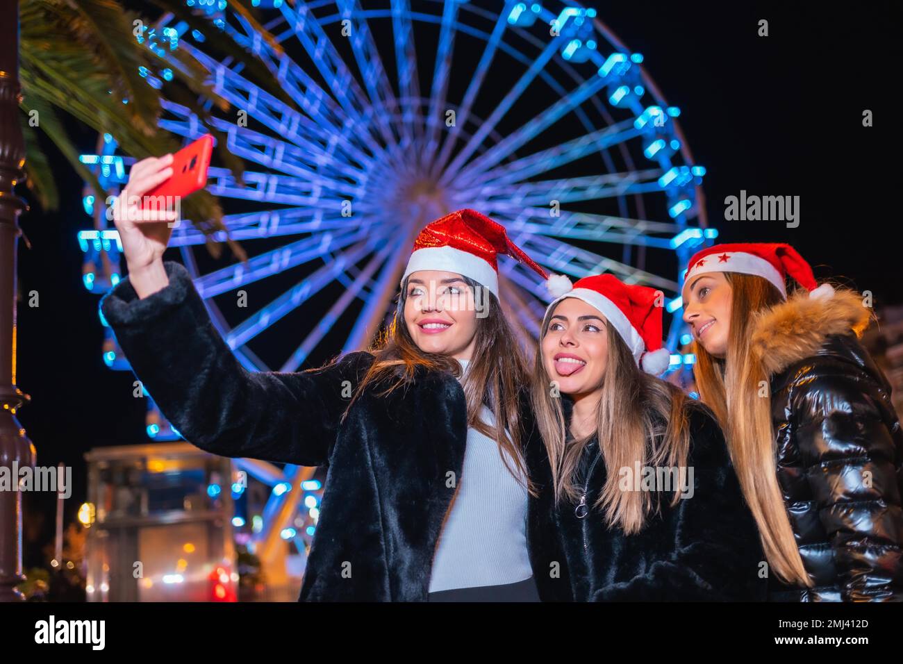 Noël dans la ville la nuit, décoration en hiver. Amis sur une grande roue illuminée prenant un selfie avec le téléphone Banque D'Images