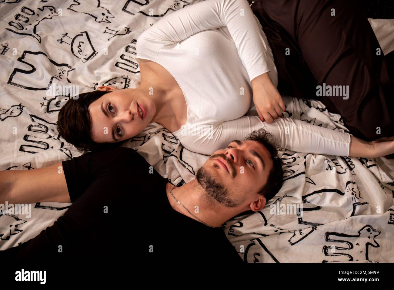 Un beau couple est couché sur le lit et regarde la caméra. Jeune couple photographié d'en haut. Banque D'Images