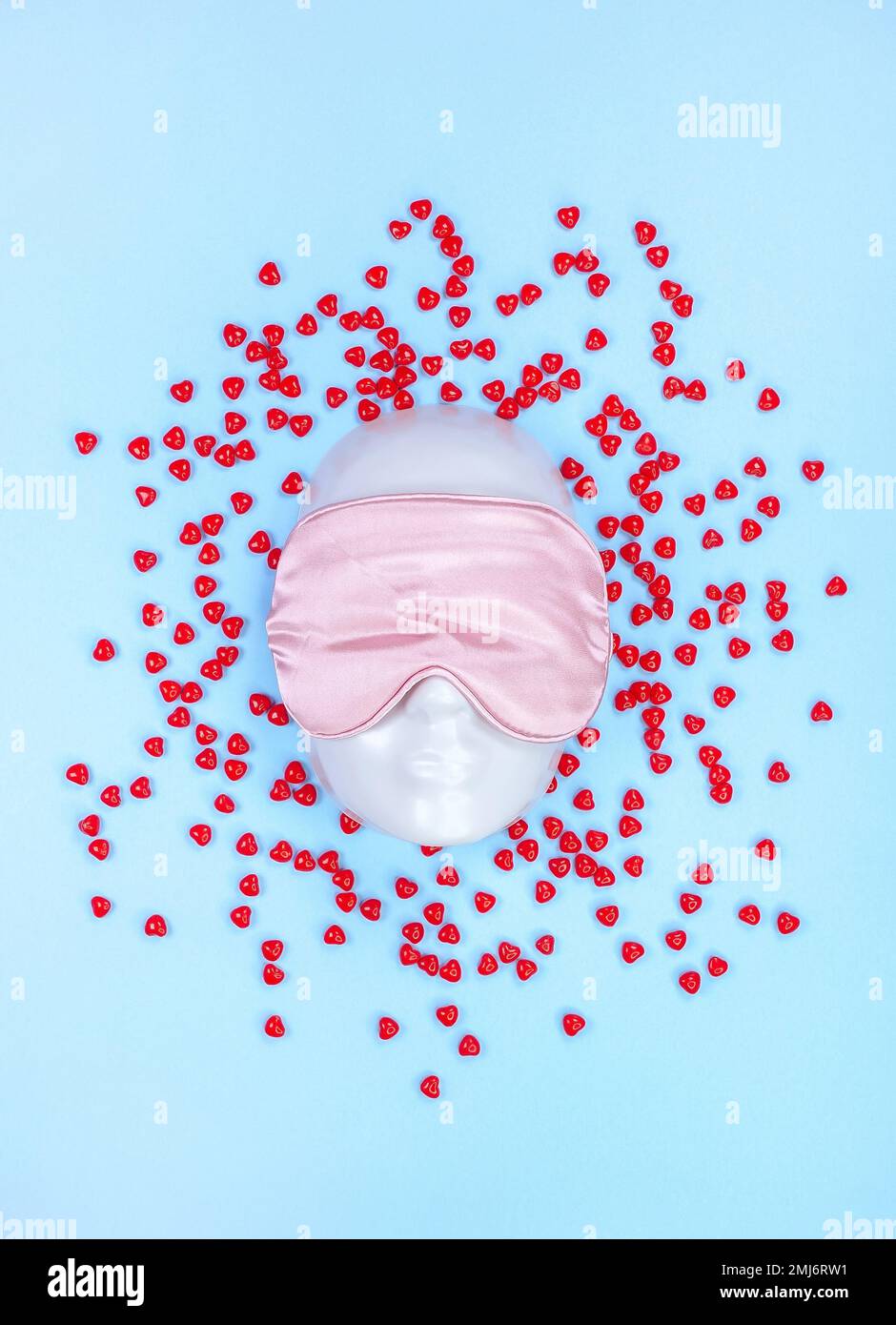 Masque de sommeil rose sur le visage du mannequin avec des bonbons rouges au cœur sur fond bleu, troubles du sommeil. Saint Valentin. Vacances, accessoire tête Banque D'Images