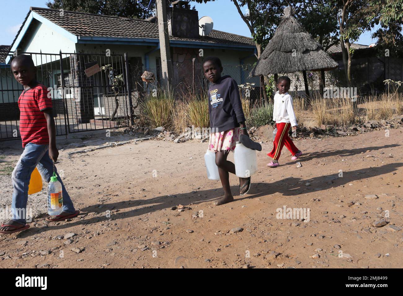 Children with containers filled with water walk past the house that
