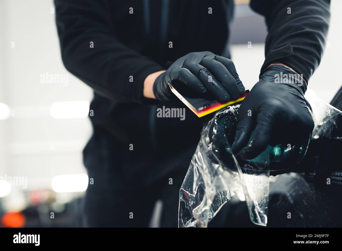 Homme méconnaissable portant des gants noirs pour lisser le film de protection de peinture PPF appliqué sur le rétroviseur latéral. Détails de voiture professionnels. Prise de vue horizontale en intérieur. Photo de haute qualité Banque D'Images