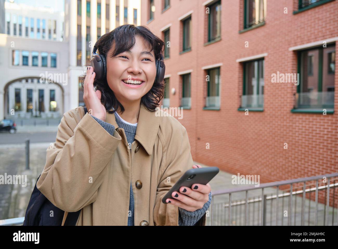 Jeune fille heureuse touriste, écoute de la musique dans les écouteurs,  boissons à emporter et vérifie le téléphone mobile, se tient dans la rue et  sourit Photo Stock - Alamy