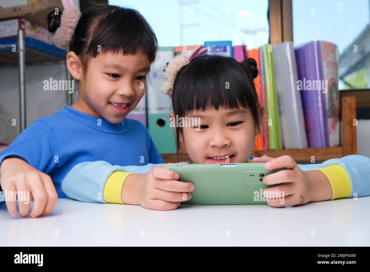 Jolie petite fille tenant un smartphone regardant l'écran souriant à l'aide d'une application, jouant à des jeux en ligne, regardant des dessins animés dans le salon à la maison. Enfant Banque D'Images