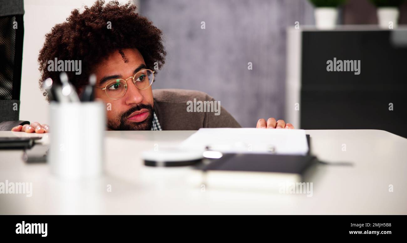 Un homme effrayé se cache derrière le bureau dans la chambre Banque D'Images