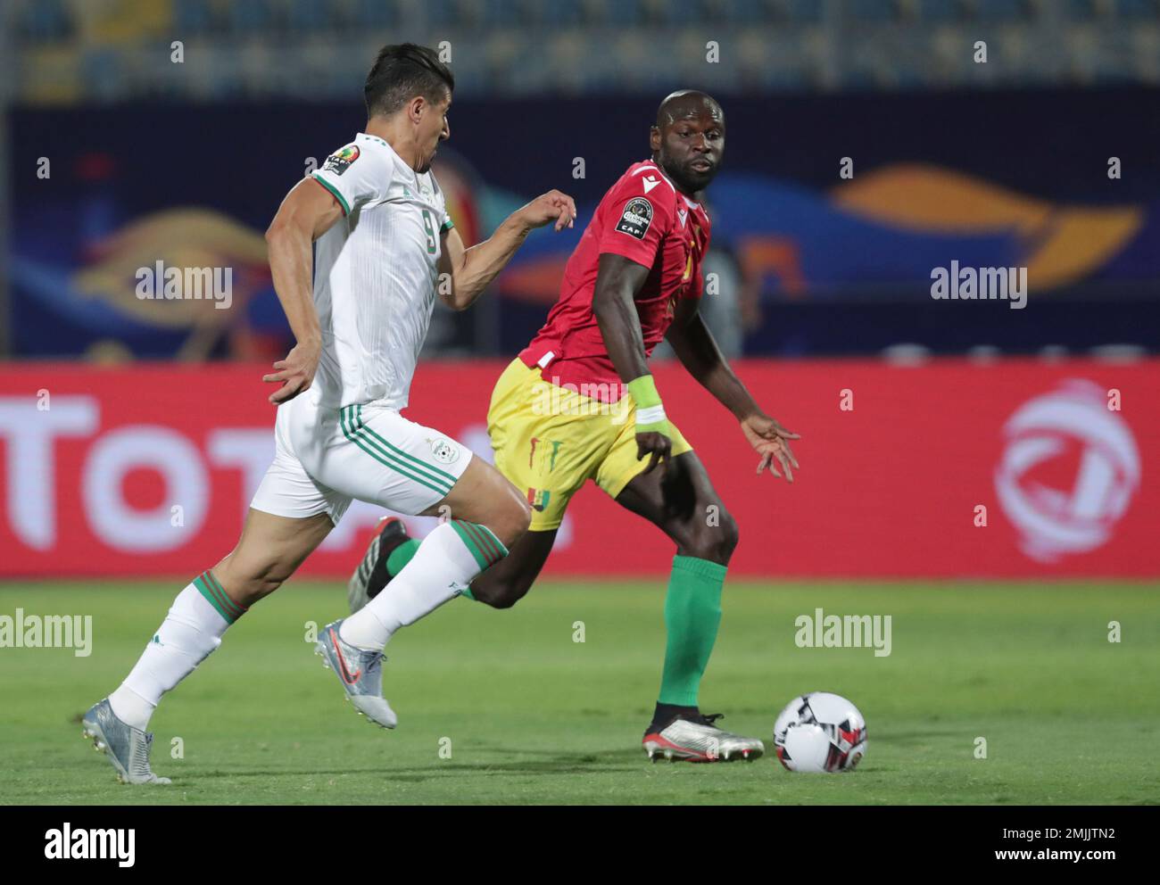 Algeria's Baghdad Bounedjah, left, and Guinea's Ernest Seka run for the ball during the African Cup of Nations round of 16 soccer match between Algeria and Guinea in 30 June stadium in Cairo, Egypt, Sunday, July 7, 2019. (AP Photo/Hassan Ammar) Banque D'Images