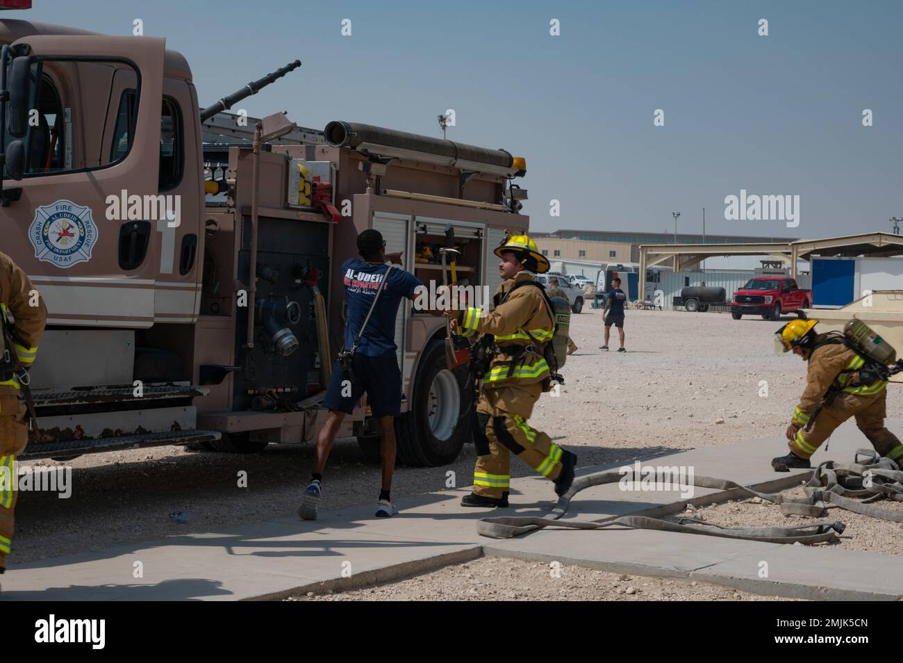 Les pompiers de l'US Air Force affectés au 379th Expeditionary civil Engineer Squadron (au centre) échangent une hache à tête plate et une barre halligan tandis qu'un autre pompier aide à étirer le tuyau à incendie (à droite) lors d'un exercice le 30 août 2022 à la base aérienne Al Udeid, Qatar. Les outils échangés entre le conducteur et l'opérateur ont été utilisés pour pénétrer de force dans des pièces scellées à l'intérieur de la structure pendant l'exercice. 379AEW, AFCENT, force aérienne, Airfighcommand, feu, usccentcom, Banque D'Images