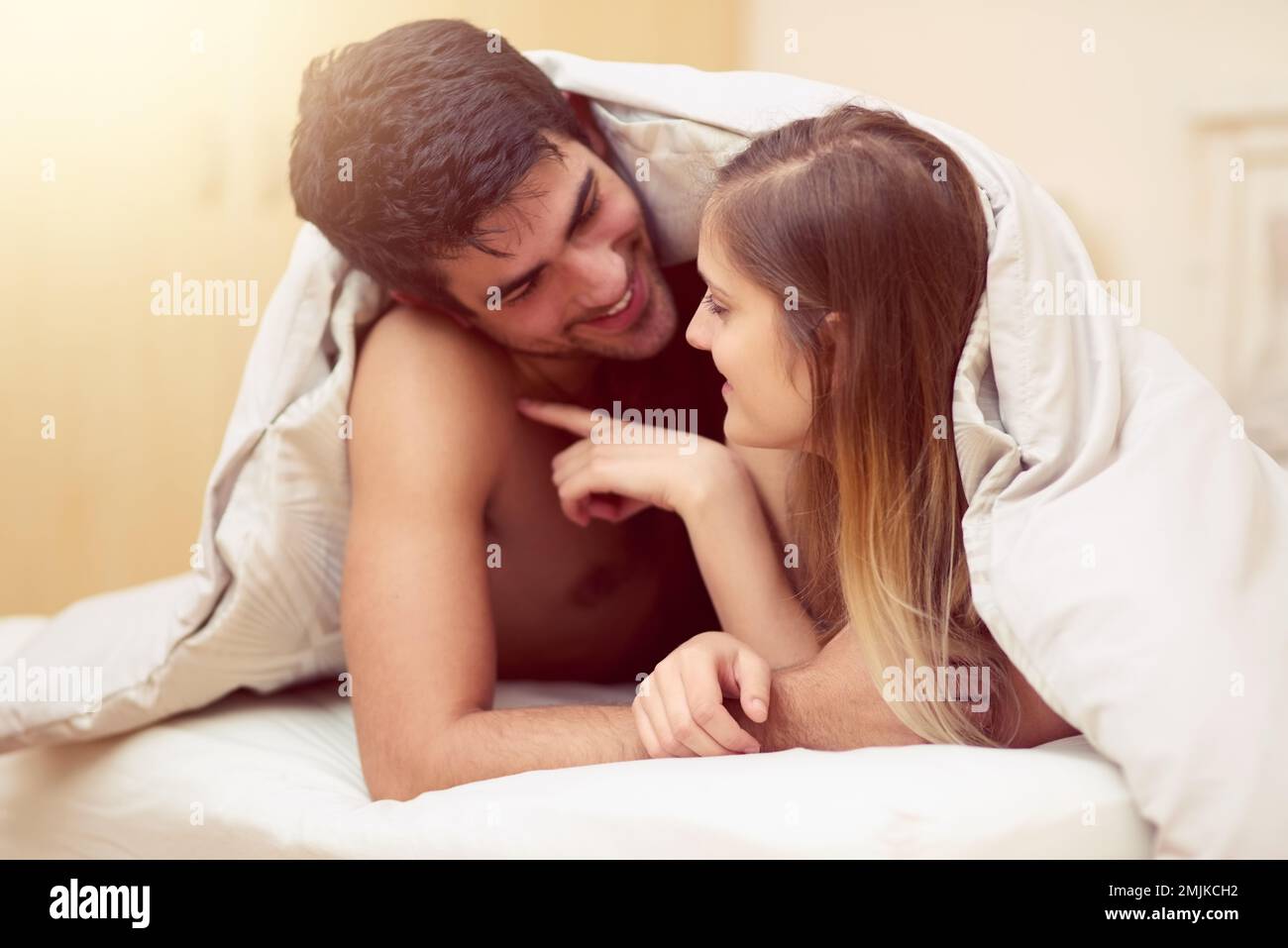Laisser ses empreintes digitales sur son coeur. un jeune couple aimant se souriant les uns les autres tout en étant allongé sous une couverture ensemble. Banque D'Images