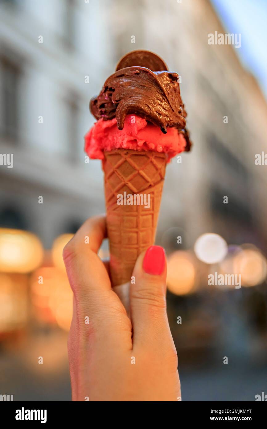 Main tenant une glace artisanale au chocolat et à la framboise, une vue sur les maisons et les lumières floues sur une rue piétonne à Centro Storico, Florence, Italie Banque D'Images