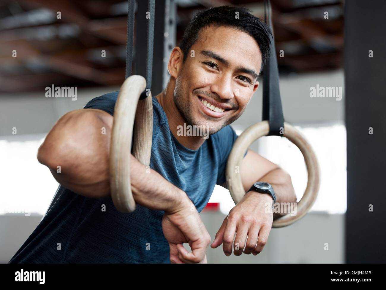 Portrait, anneaux de gymnastique et jeux olympiques avec un homme gymnaste accroché à l'équipement pour l'entraînement en salle de gym. Visage, fitness et exercice avec un athlète masculin Banque D'Images
