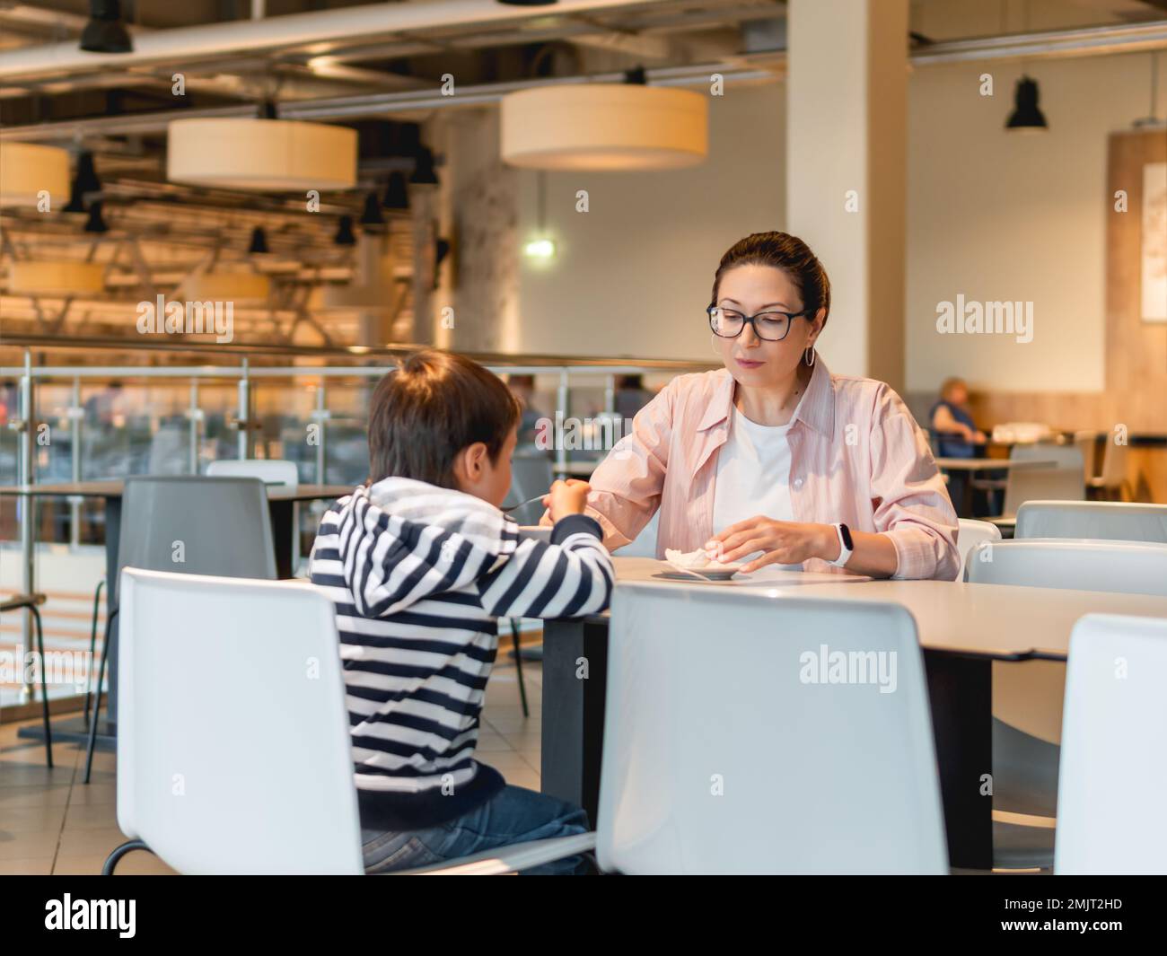 Mère et fils mangent au café. Famille sur l'aire de restauration dans le centre commercial. Femme et enfant déjeunent dans une cafétéria moderne et méconnaissable. Banque D'Images