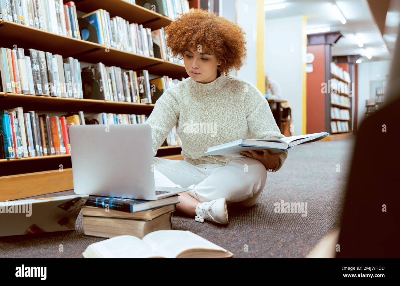 Apprentissage étudiant, recherche sur ordinateur portable et femme noire en bibliothèque travaillant sur le sol avec des livres. Lecture, recherche informatique et étude en ligne d'une personne Banque D'Images
