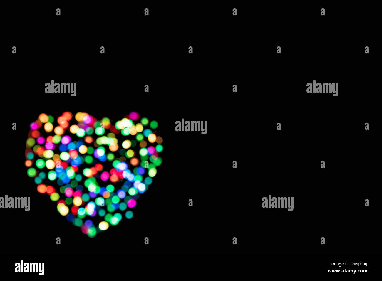 Cercles multicolores en forme de coeur clair avec effet bokeh sur fond noir et espace de copie (toile de fond pour le jour de la Saint-Valentin) Banque D'Images