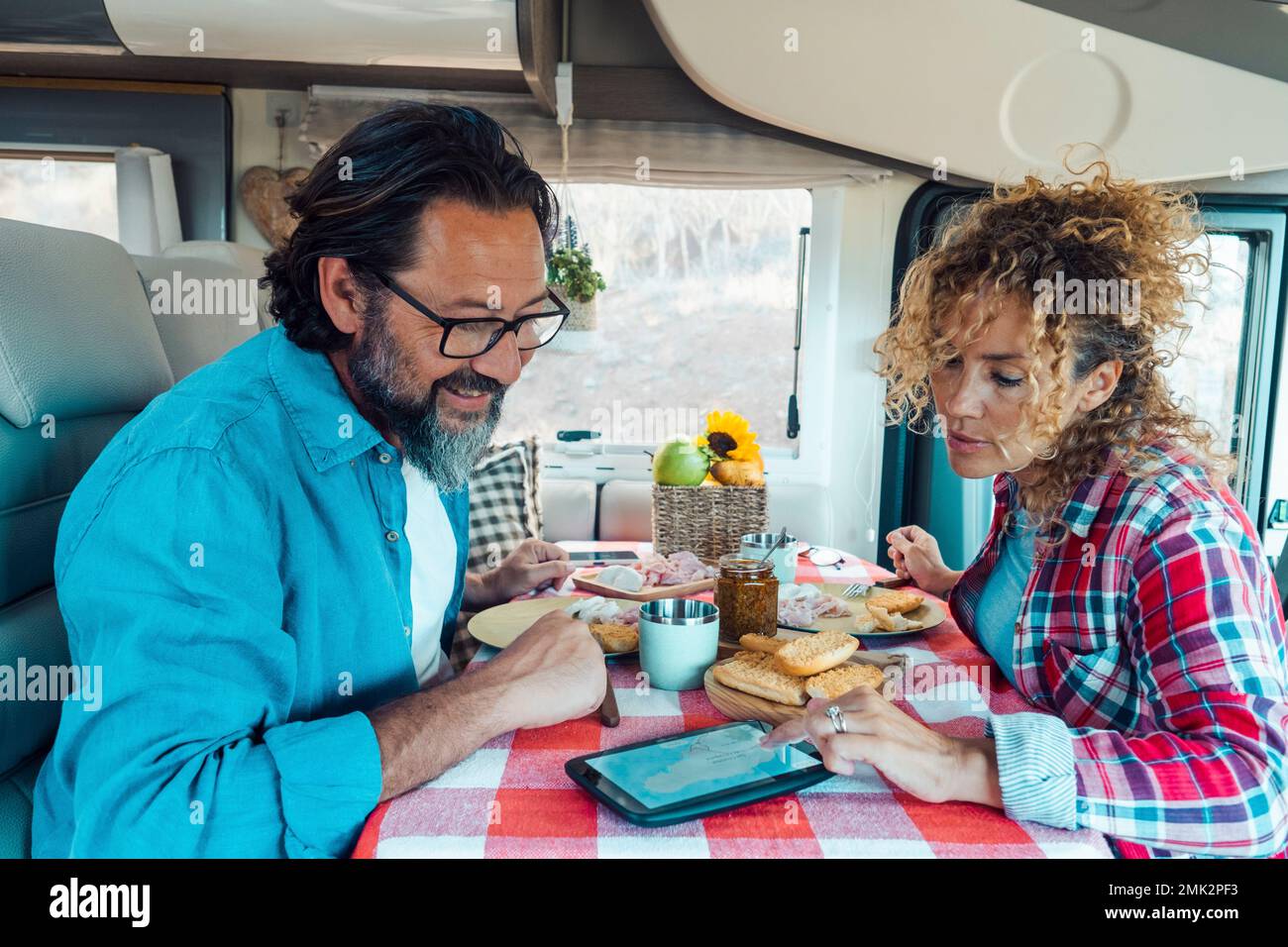 Couple homme et femme à l'intérieur d'une camionnette de camping-car planifiant la prochaine destination de voyage ensemble à l'aide d'un gps moderne sur la table. Déjeuner sur le moteur du véhicule h Banque D'Images