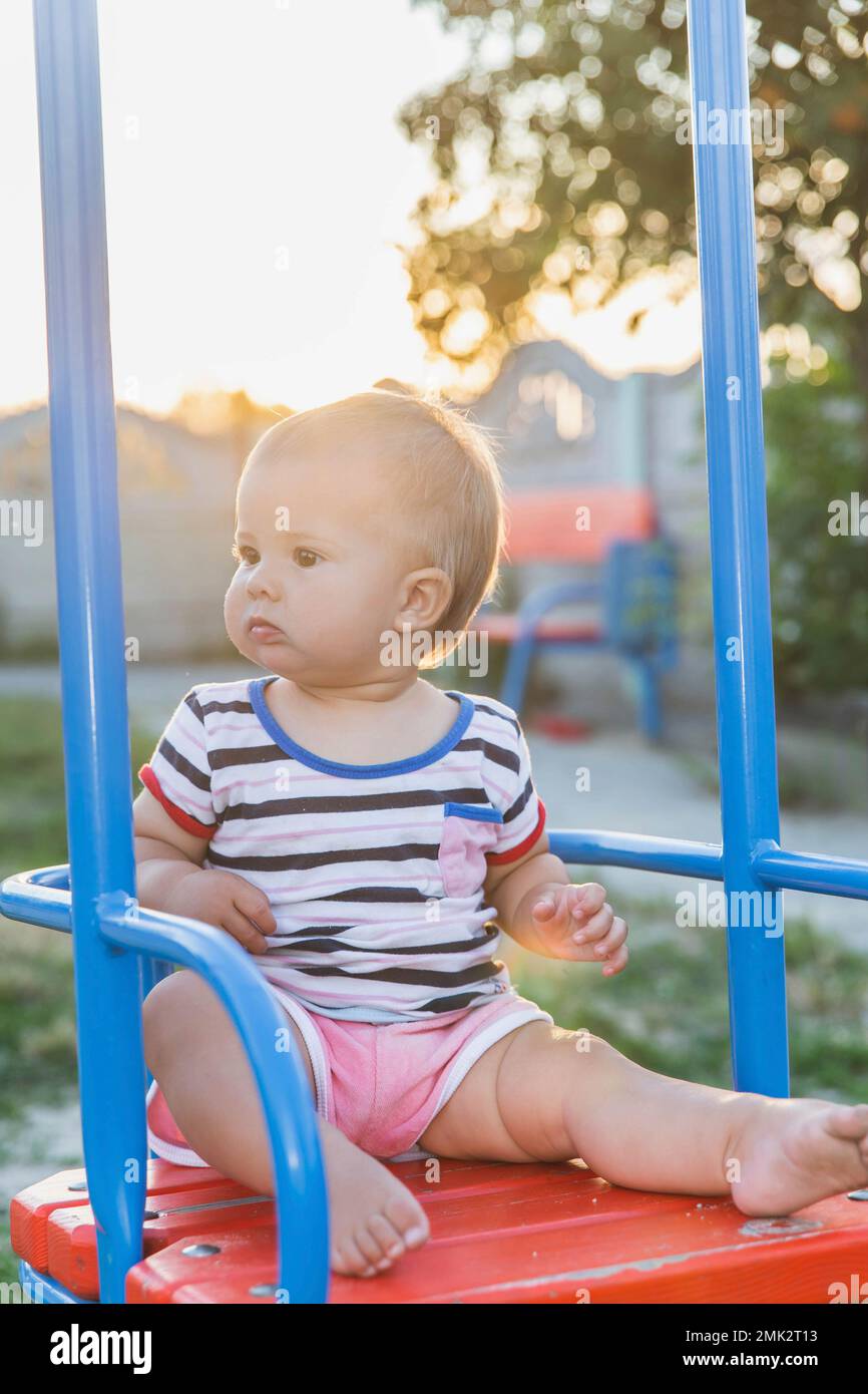 Bébé blond assis sur une balançoire au coucher du soleil Banque D'Images