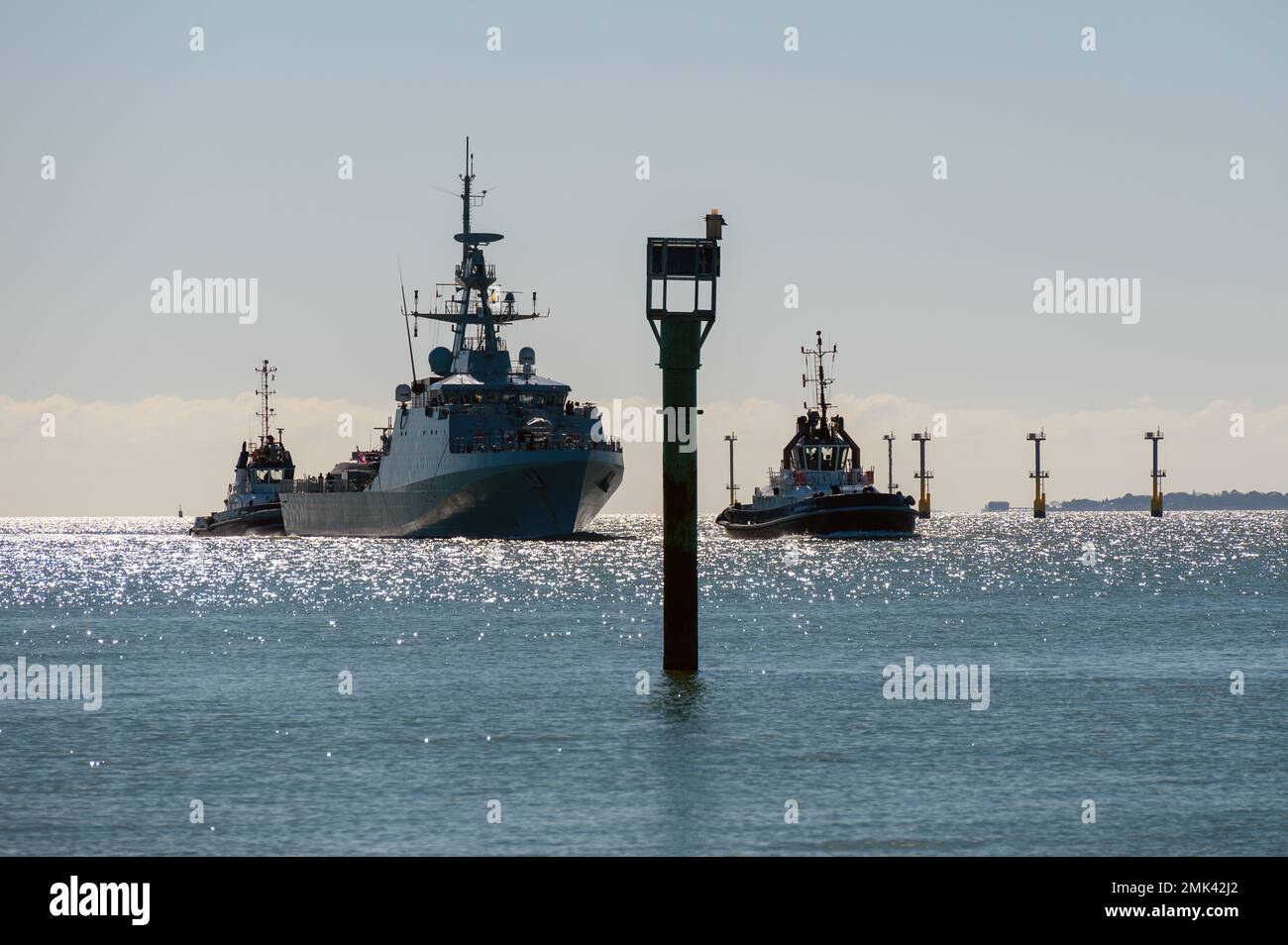 Vue rétroéclairé des remorqueurs de Serco Marine qui guident le navire de patrouille maritime de la Royal Navy dans le port. Banque D'Images