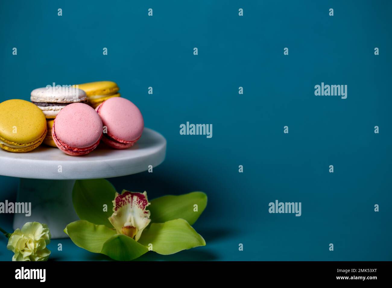 Des gâteaux de macaron français sur un gâteau blanc marbel se dressent sur fond bleu. Macarons jaunes blancs et roses. Orchidée et sauge. Banque D'Images