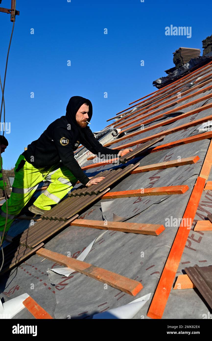 Couvreur posant des carreaux sur de nouvelles matraques au-dessus d'une membrane de ventilation sur le toit de maison de rénovation, Royaume-Uni Banque D'Images