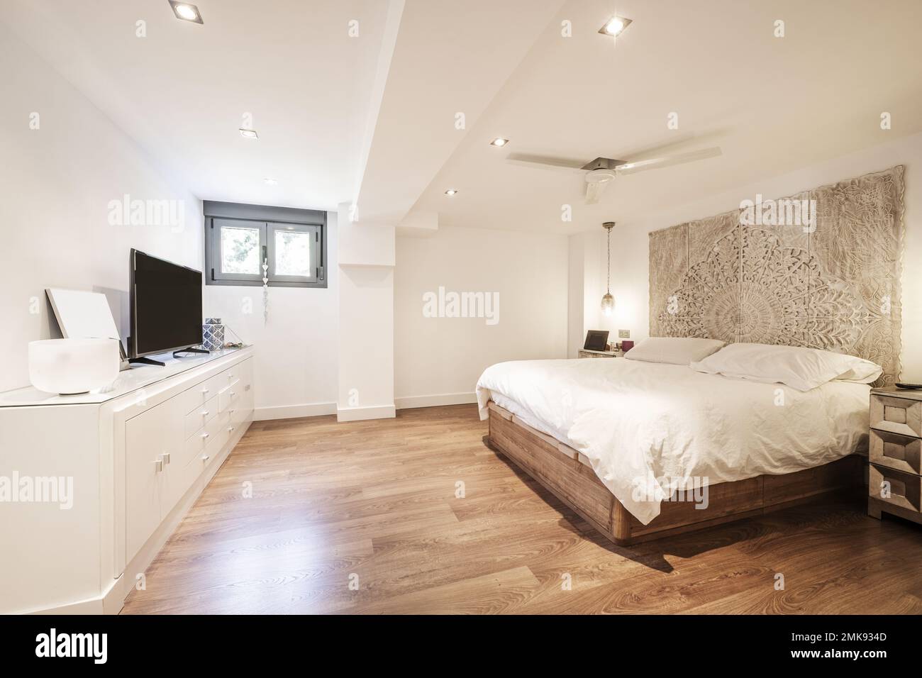 Chambre avec lit double avec couette blanche, parquet en bois sombre, tête de lit en bois de mandala, grand buffet blanc laqué en bois et petite connexion wi Banque D'Images