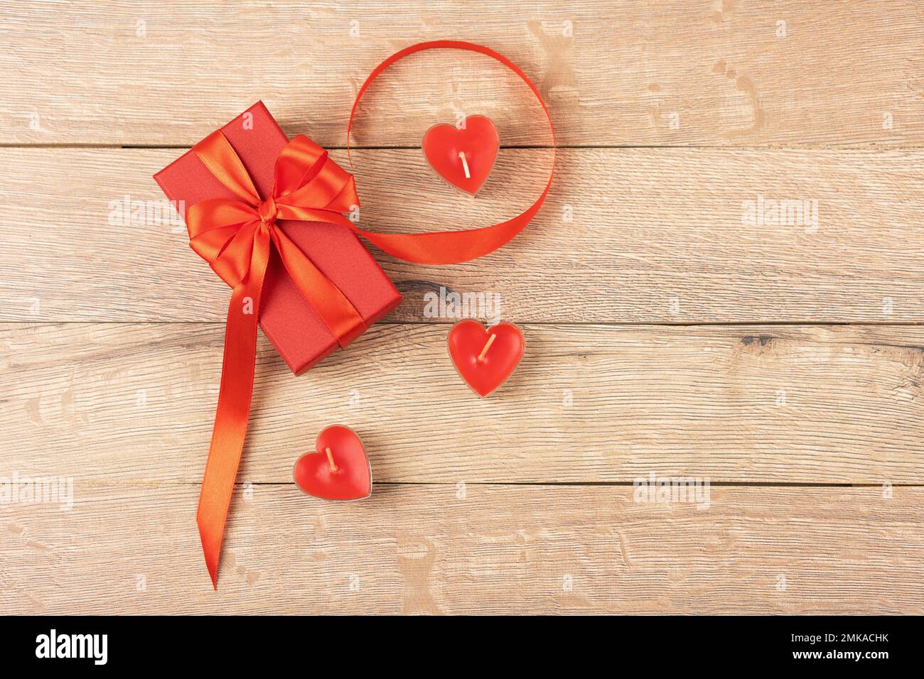 Boîte cadeau rouge avec un noeud en ruban de satin rouge et des bougies rouges en forme de coeur sur un fond en bois. Bonne Saint Valentin, fête des mères et naissance Banque D'Images