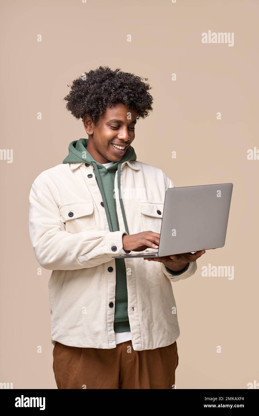 Un étudiant afro-américain souriant utilisant un ordinateur portable isolé sur fond beige. Banque D'Images