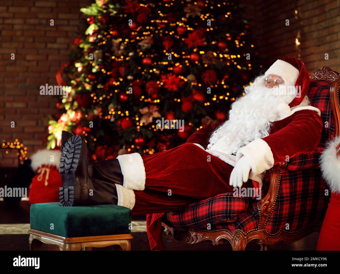 Le Père Noël repose dans un fauteuil près d'un arbre de Noël décoré à l'intérieur Banque D'Images